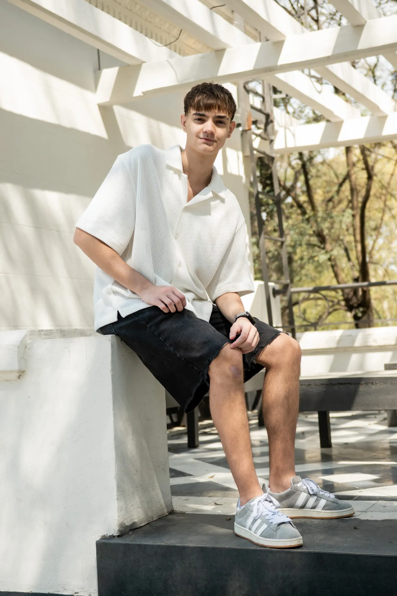 Facundo sentado en una pérgola blanca, con camisa blanca y bermuda negra